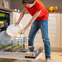 Kind räumt Geschirr in die Spülmaschine